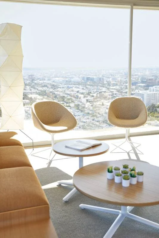 Oatmeal lounge chairs around a round table by city-view windows