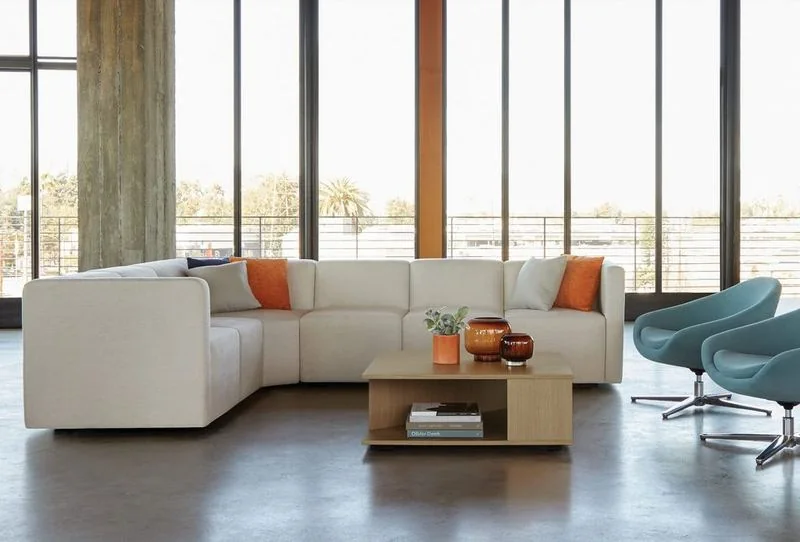 White sectional with orange pillows and blue swivel chairs by tall windows