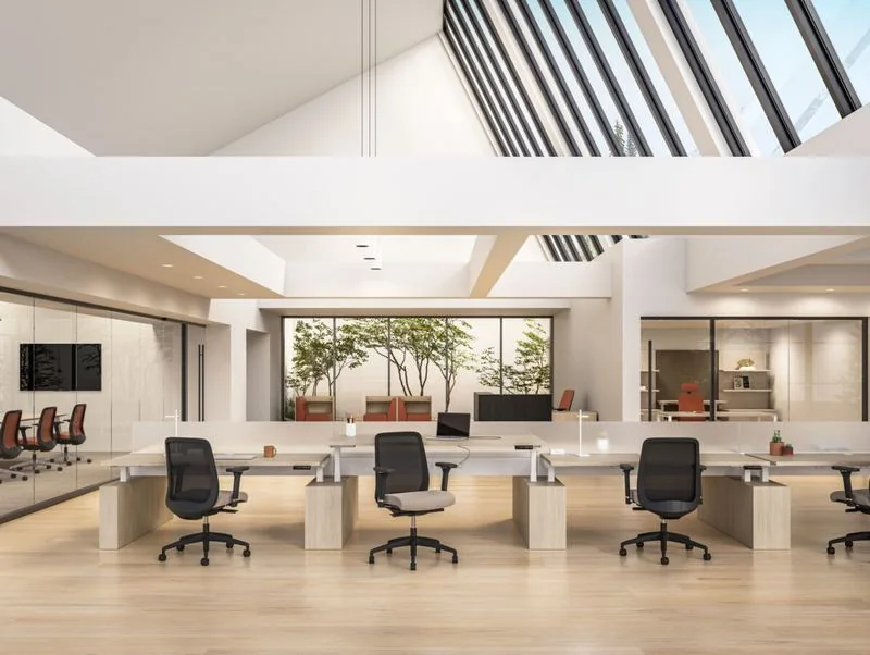 Benching Open-plan benching with light wood desks under a sawtooth skylight